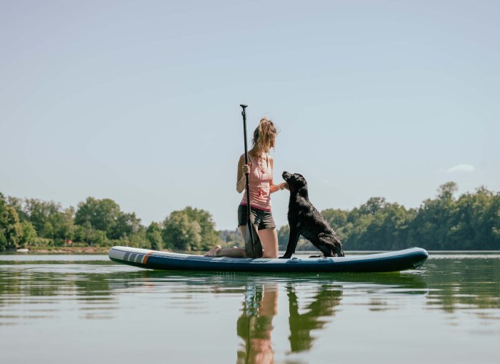 A woman paddle boarding with a dog in a river